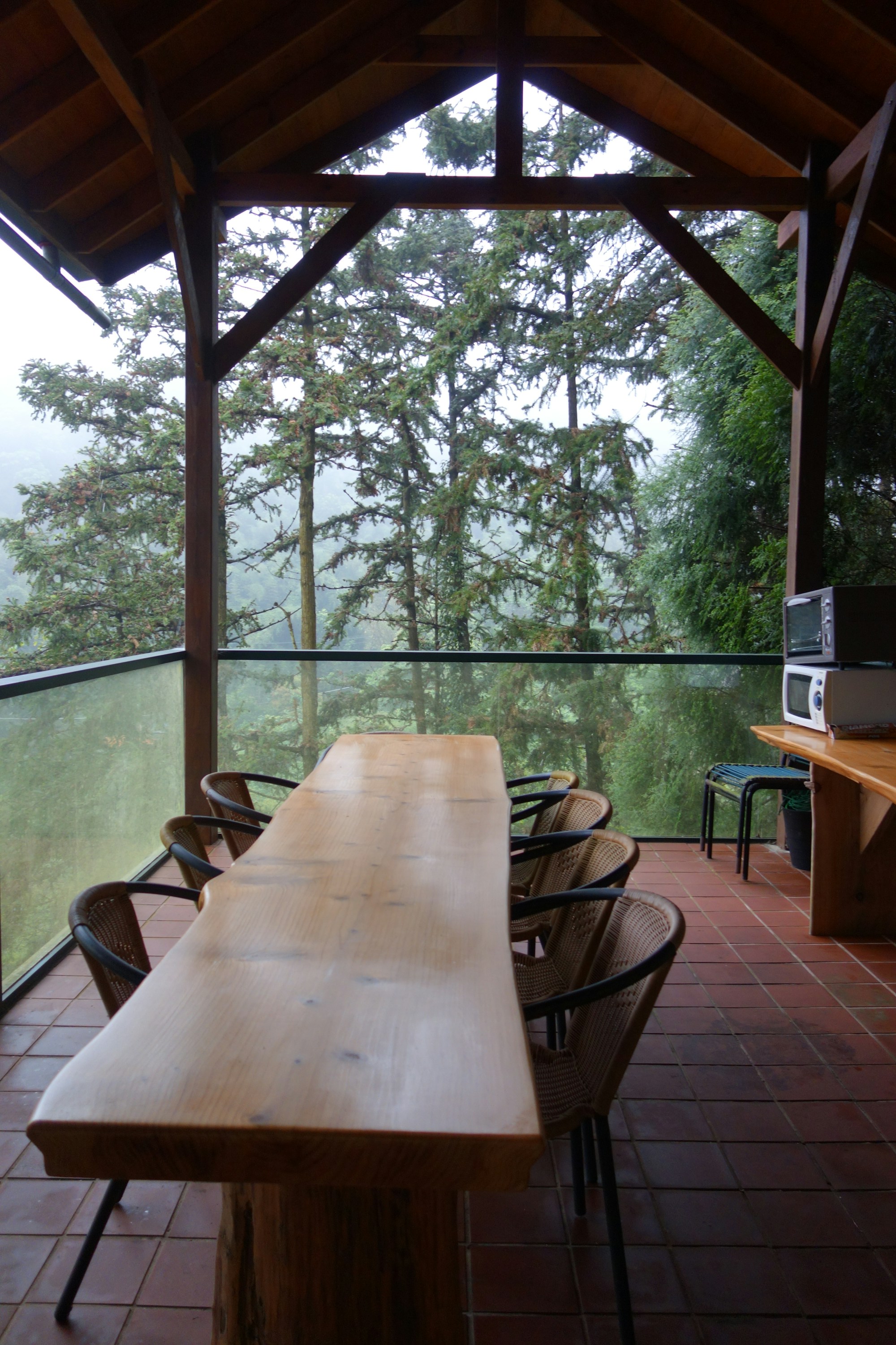 A timber table and chairs on a covered deck looking out into the trees.